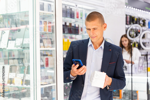 Smiling elegant young man standing in tech store with new smart phone in his hands © JackF