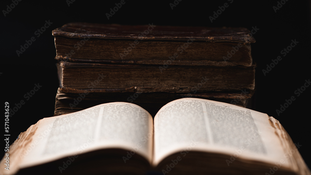 Open blurred Torah page and old worn shabby jewish books in leather binding in the background. Closeup. Selective focus.