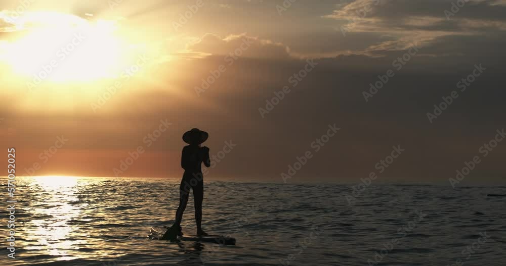 A girl in a hat stands on a swimming board with an oar in her hands against the background of the morning sun, summer vacation at the sea. A girl in a hat stands on a swimming board with an oar in her hands against the background of the morning sun, summer vacation at the sea.