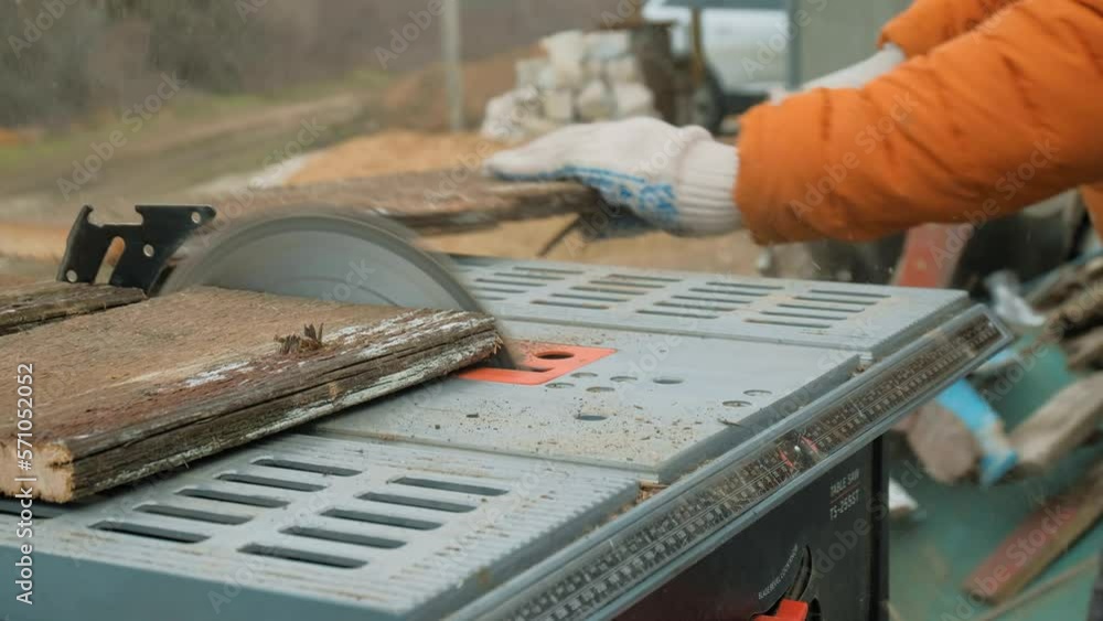 Man In Gloves Cutting A Wooden Plank With Table Saw Man In Gloves Cutting A Wooden Plank With Table Saw