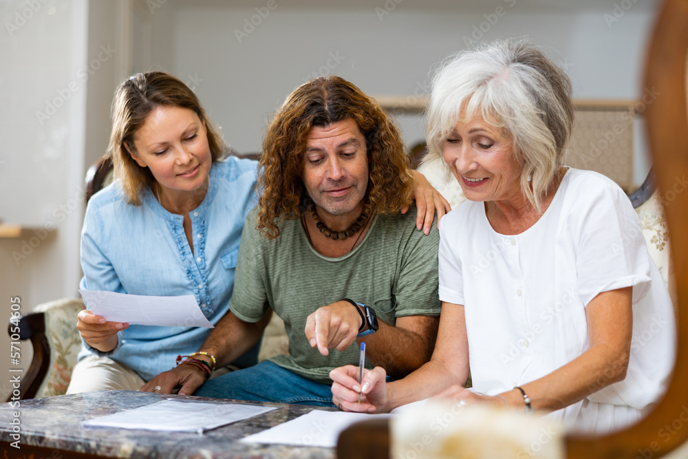 Obraz premium Mature mother and adult children fill out paperwork in home room