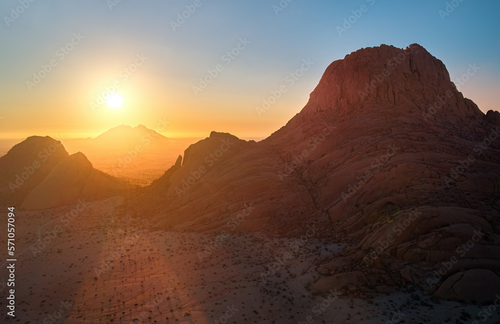 Aerial view of a  Spitzkoppe mountain, area of red, bald granite peaks against setting sun. Rocky desert landscape. Hiking paradise, remote place, Namib desert, Namibia. 