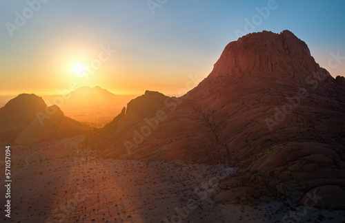 Aerial view of a Spitzkoppe mountain, area of red, bald granite peaks against setting sun. Rocky desert landscape. Hiking paradise, remote place, Namib desert, Namibia. 