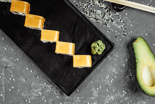 Traditional fresh japanese sushi rolls on a black stone Teka Kaji. Roll ingredients: cheese cheder, philadelphia cheese, cucumber, tuna chips, nori, rice photo