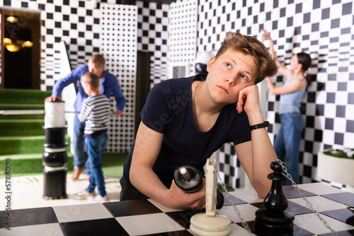Portrait of thoughtful teenage boy trying to find solution of conundrum in quest room stylized under chessboard