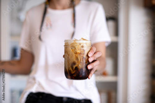 person holding iced coffee with cream poured