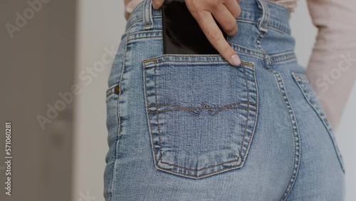 Close up shot of unrecognizable women's hand put mobile phone into her trendy blue jeans pocket, back view, empty space