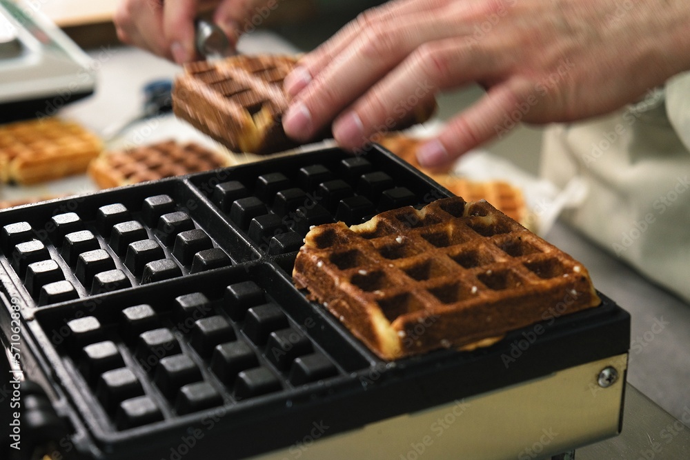 belgian waffles in a waffle iron. the cook pulls the finished Belgian waffles out of the oven belgian waffles in a waffle iron. the cook pulls the finished Belgian waffles out of the oven