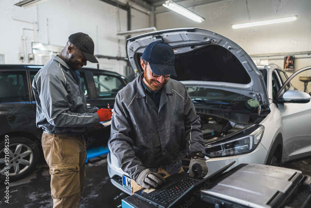 two professional servicemen making car diagnostics on a laptop and smiling, medium shot car repair shop. High quality photo two professional servicemen making car diagnostics on a laptop and smiling, medium shot car repair shop. High quality photo