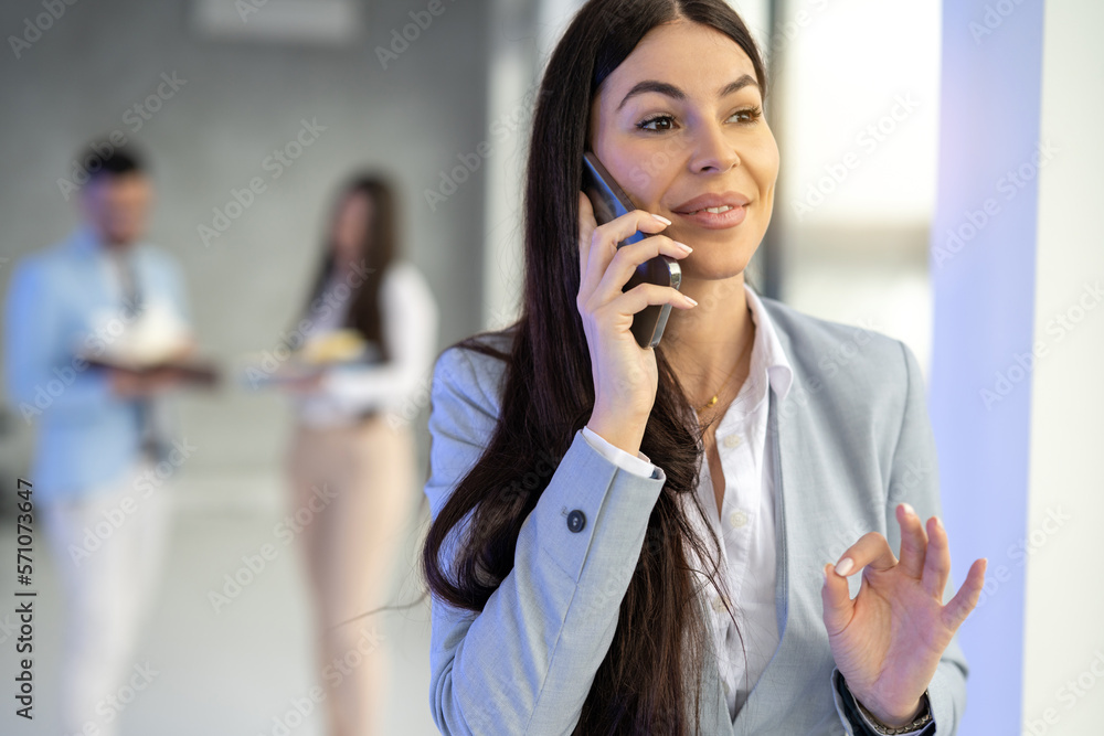 Portrait of beautiful surprised business woman talking on mobile phone gesturing okey sign with hand at office. Portrait of beautiful surprised business woman talking on mobile phone gesturing okey sign with hand at office.