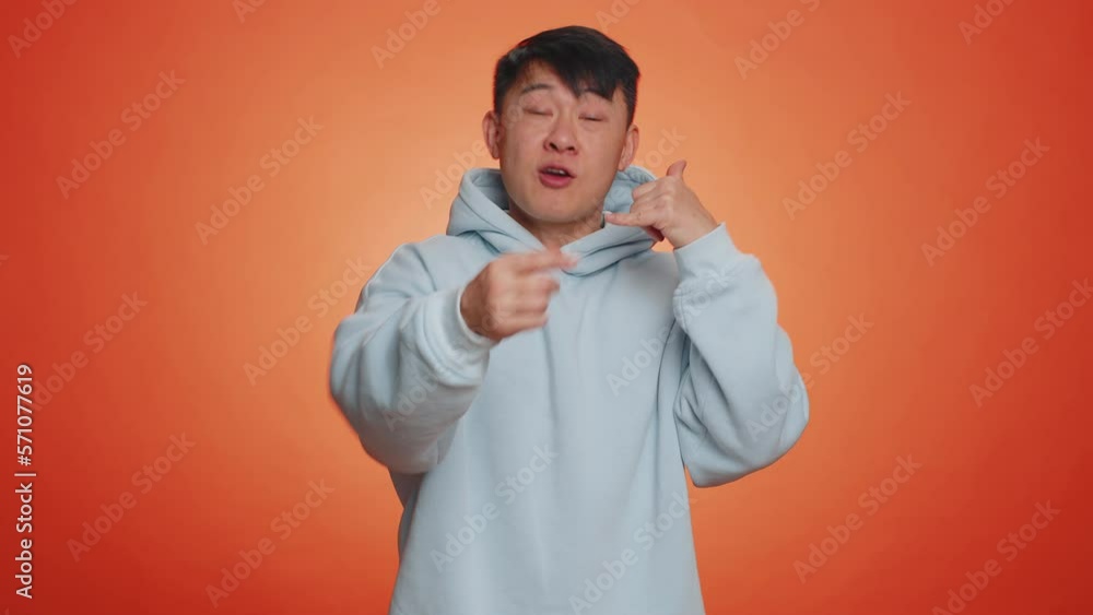 Call us, here is contact number. Handsome asian man in hoodie looking at camera doing phone gesture like says hey you call me back, conversation. Chinese guy isolated on orange background, indoors Call us, here is contact number. Handsome asian man in hoodie looking at camera doing phone gesture like says hey you call me back, conversation. Chinese guy isolated on orange background, indoors