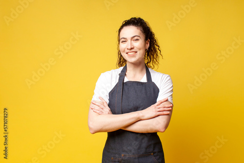 portrait of young barista girl in uniform on a yellow background, a woman waiter stands with crossed arms photo