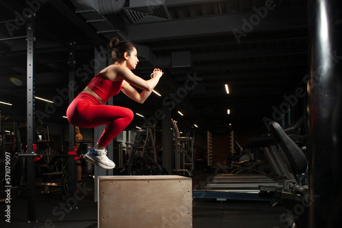 young athletic girl in red sportswear jumping in black gym, attractive woman doing sports in the fitness room © Богдан Маліцький