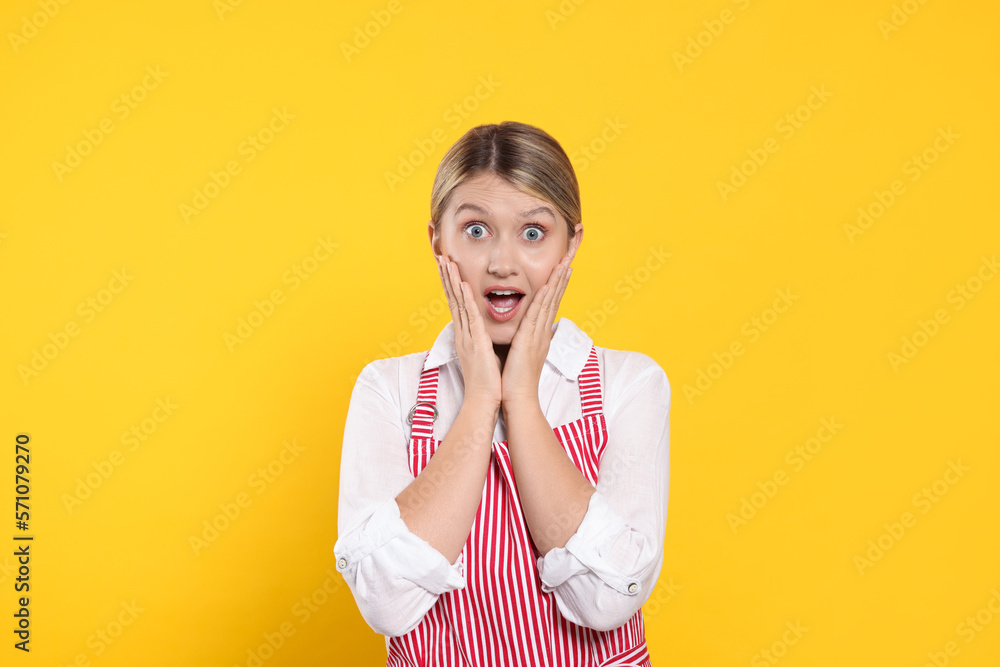 Beautiful young woman in clean striped apron on orange background Beautiful young woman in clean striped apron on orange background
