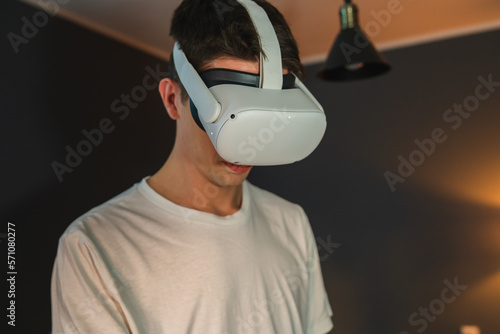 A young guy is wearing virtual reality or oculus head set and playing in virtual reality in his room
