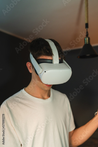A young guy is wearing virtual reality or oculus head set and playing in virtual reality in his room