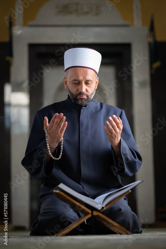 Photography A Muslim prayer man praying with hands up while reading a Quran inside the mosque
