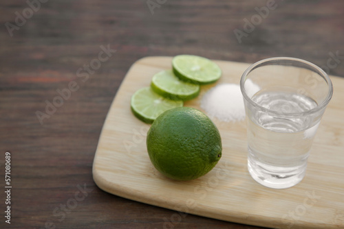 Mexican tequila shot with lime slices on wooden table, closeup and space for text. Drink made from agave