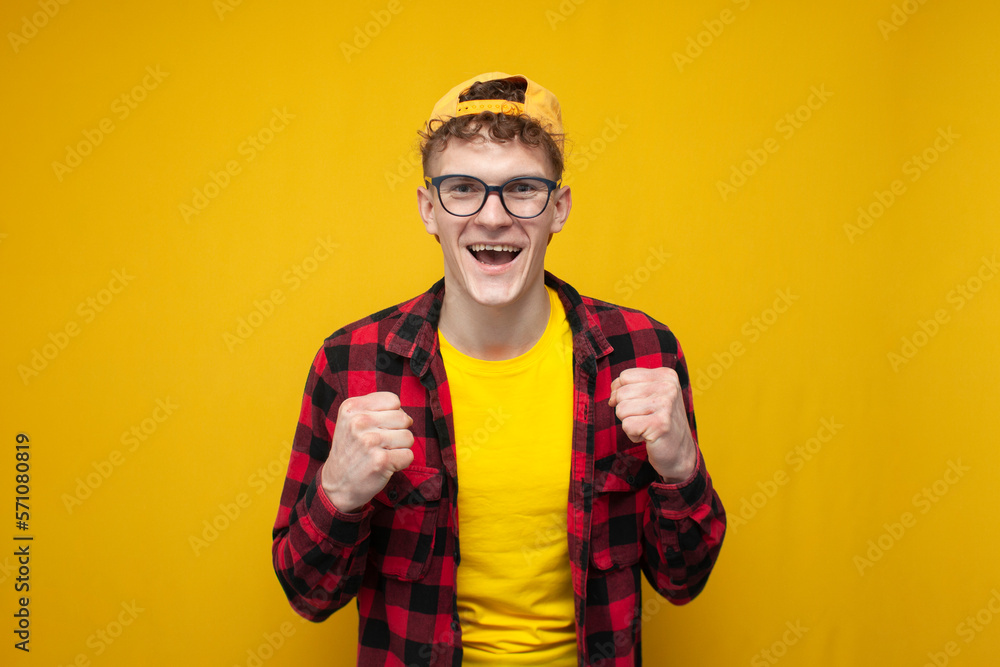 curly guy with glasses wins and rejoices in victory, the student shows the emotion of victory on a yellow background curly guy with glasses wins and rejoices in victory, the student shows the emotion of victory on a yellow background