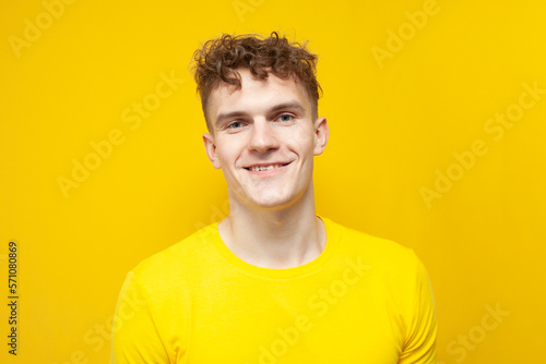 portrait of a young curly guy in a yellow T-shirt on a yellow background