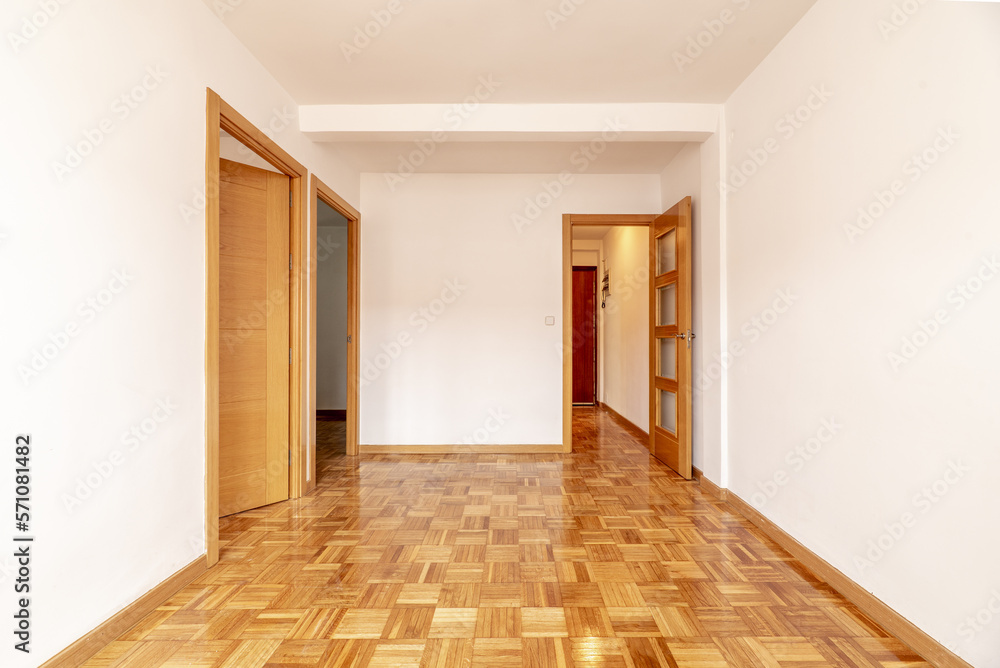 Empty living room of an apartment with parquet flooring of freshly stabbed and varnished oak slats and wooden doors of the same material - obrazy, fototapety, plakaty 