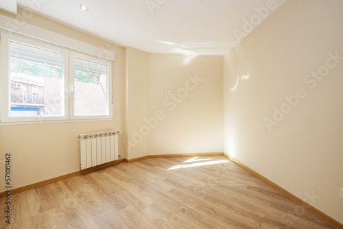 Empty living room with oak laminate flooring, cream painted walls and aluminum window over a white radiator