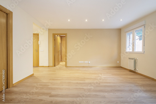 Empty one-story living room with floating oak flooring  access doors to other rooms  integrated lamps in the false plaster ceiling and white aluminum windows