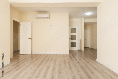 Empty living room with woodwork with white doors and moldings, air conditioners and radiators in the same color and walls painted in vanilla color