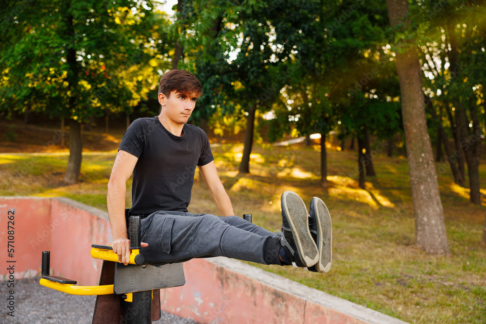 Young man doing fitness exercises on a special hanging device. Fitness male guy doing exercising with suspension trainer slingin a city park. A suspended TRX sport fitness concept.