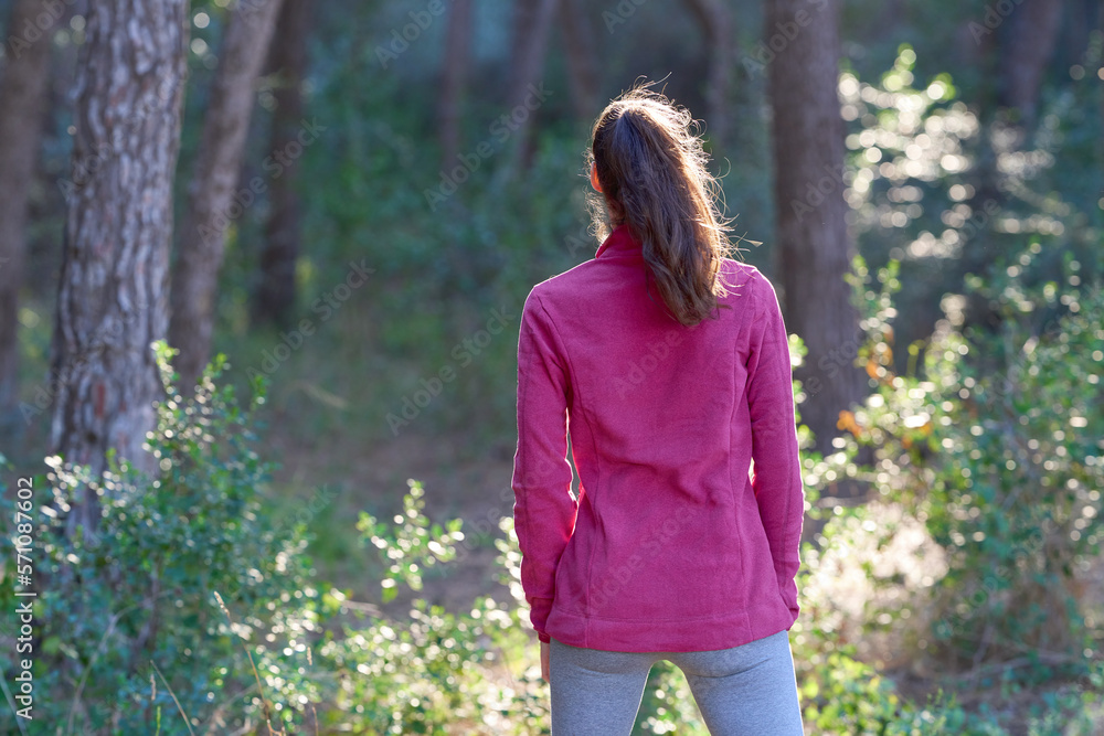 woman seen from behind walking through the forest with a pink sweatshirt