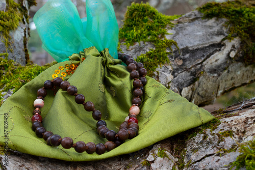 A close up image of wooden prayer beads and a green silk pouch resting on a moss covered tree branch. 