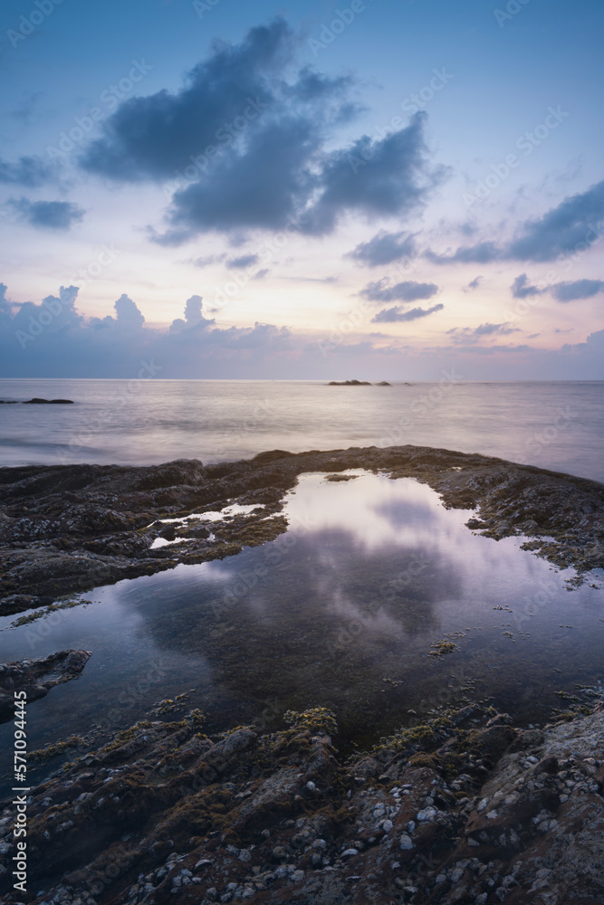 vertical photo of a sea sunset and rocks. The dramatic evening sky is reflected in the seawater coast nature of thailand phuket kaolak