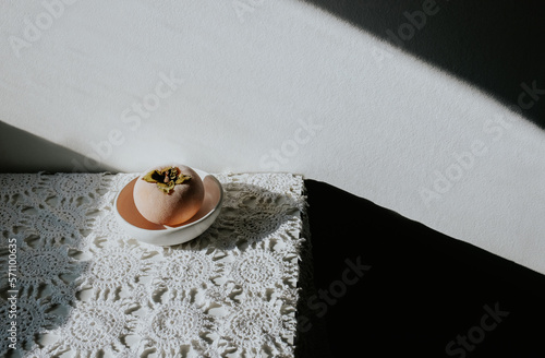 A frozen persimmon sits in a white bowl on a white tablecloth.