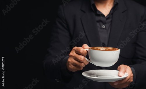 Businessman in a suit is holding a cup of coffee while standing on a black background