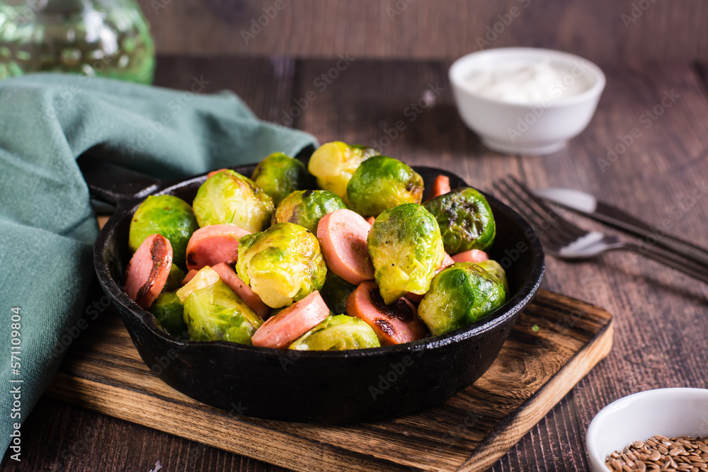 Roasted brussels sprouts with sausages in a frying pan on the table. Home dinner.