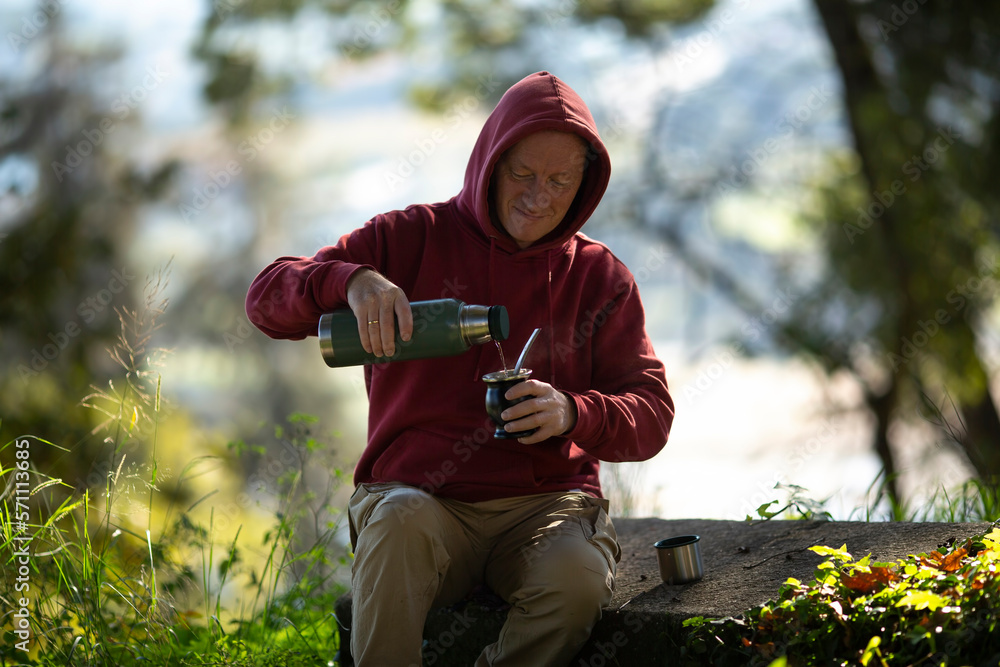 A man pours mate from a thermos into a mug in the park.