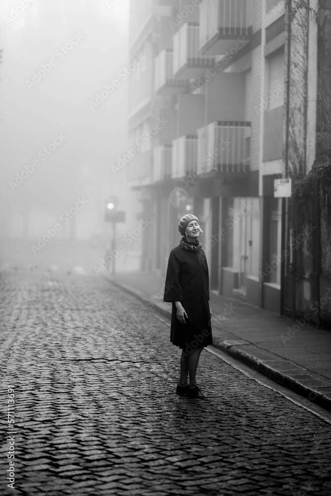 A woman enjoys on a deserted street in the thick fall morning fog. Black and white photo.