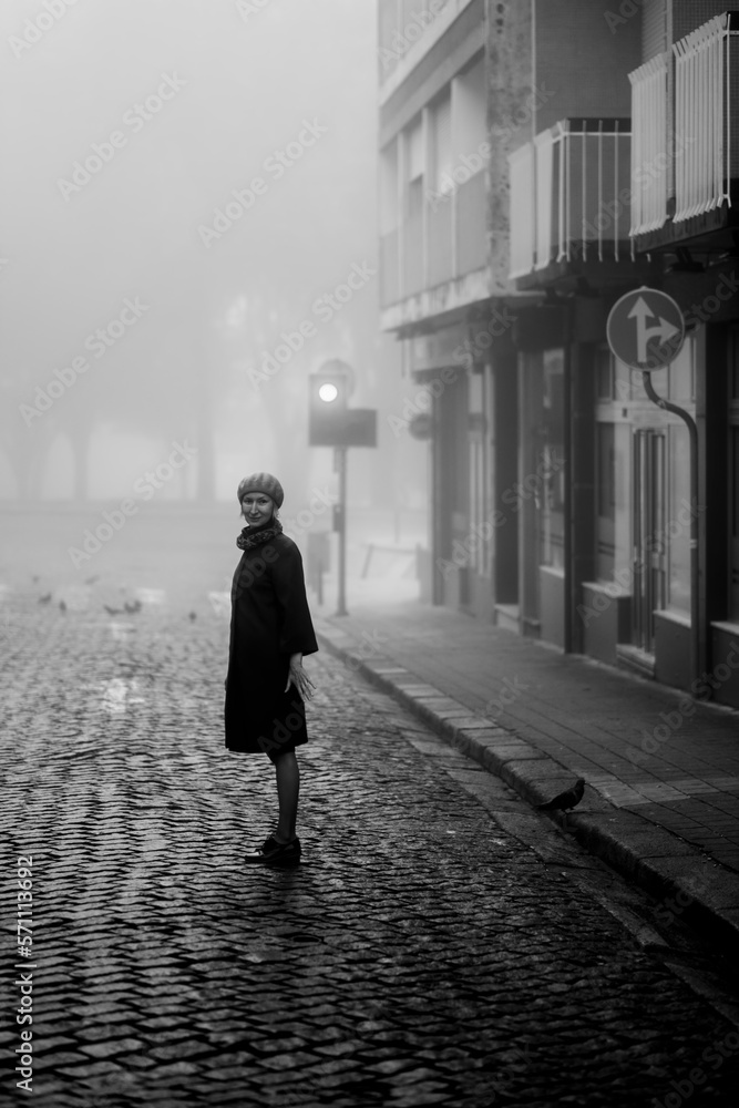 A woman on a deserted street in the thick fall morning fog. Black and white photo.