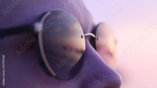 Young man in sunglasses looks at the sunset standing on a sandy beach by the sea.