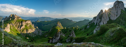 Panorama of green meadow with rocks and rocky mountains in romanian mountains in muntii ciucas with setting sun