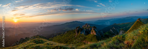 Panorama of green meadow with rocks and rocky mountains in romanian mountains in muntii ciucas with raising sun photo