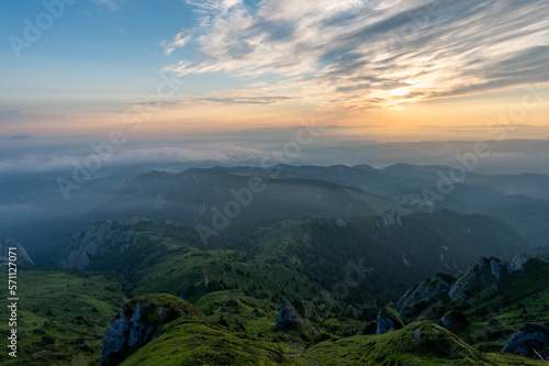 Fototapeta Naklejka Na Ścianę i Meble -  Panorama of green meadow with rocks and rocky mountains in romanian mountains in muntii ciucas with raising sun