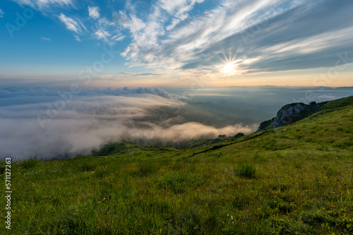 Green meadows with rocks and rocky mountains with fog in the valley and clouds in the sky in romanian mountains in muntii ciucas photo