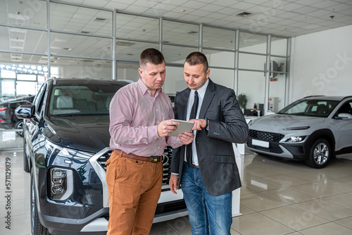 professional consultant provides all information about a new car using a tablet to his client © RomanR