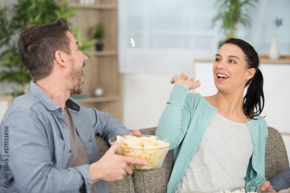 couple with chips sitting on the sofa laughing couple with chips sitting on the sofa laughing
