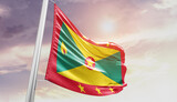 Waving Flag of Grenada in Blue Sky. The symbol of the state on wavy cotton fabric.