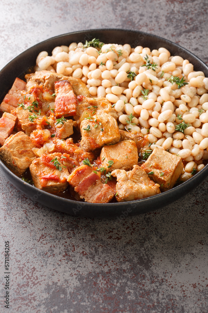 Slowly stewed pork with bacon, tomato and onion served with a side dish of white beans close-up in a plate on the table. Vertical Slowly stewed pork with bacon, tomato and onion served with a side dish of white beans close-up in a plate on the table. Vertical