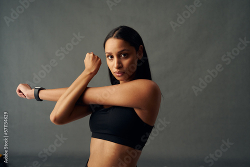 Young biracial woman in sports bra looking at camera while doing cross arm stretch in studio © StratfordProductions