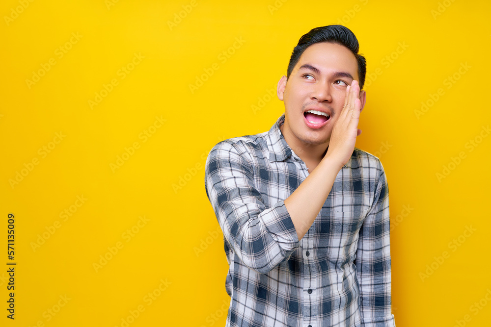 Smiling young handsome Asian man hand on mouth telling secret and whispering gossip isolated on yellow background. People lifestyle concept Smiling young handsome Asian man hand on mouth telling secret and whispering gossip isolated on yellow background. People lifestyle concept