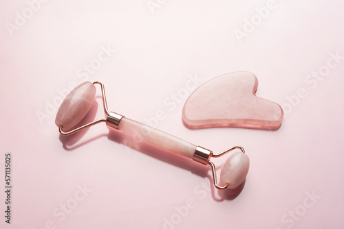 Close-up quartz roller and gua sha massage scraper on pink background. Facial massage tools. Skin care, beauty and health concept.